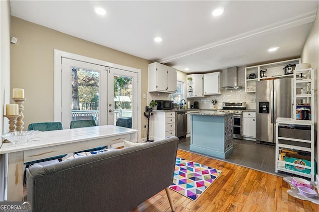 kitchen with wall chimney range hood, white cabinetry, stainless steel appliances, a kitchen island, and dark hardwood / wood-style flooring