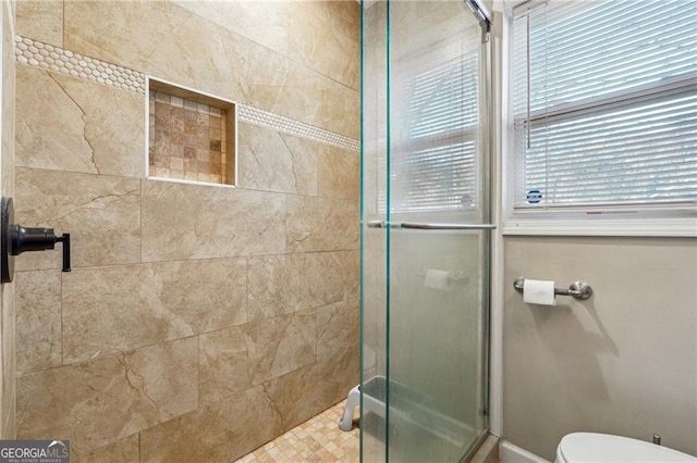 bathroom featuring a shower with door and toilet