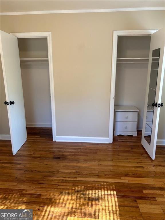 unfurnished bedroom featuring ornamental molding, dark hardwood / wood-style floors, and two closets