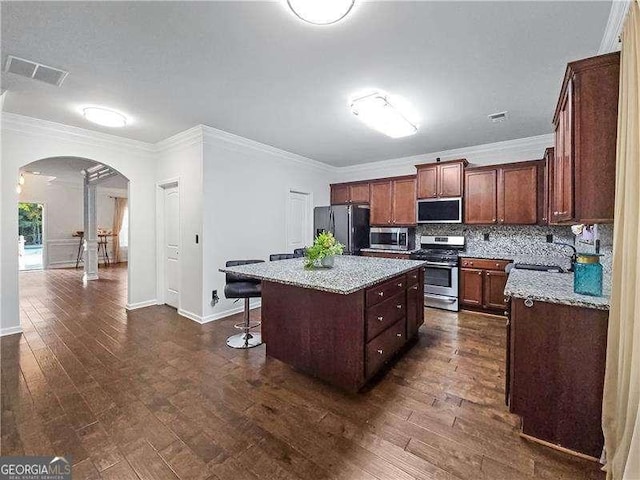 kitchen with a center island, light stone counters, ornamental molding, and stainless steel appliances