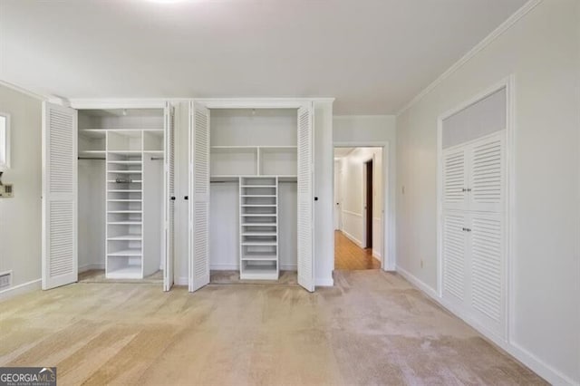 unfurnished bedroom with ornamental molding, two closets, and light colored carpet