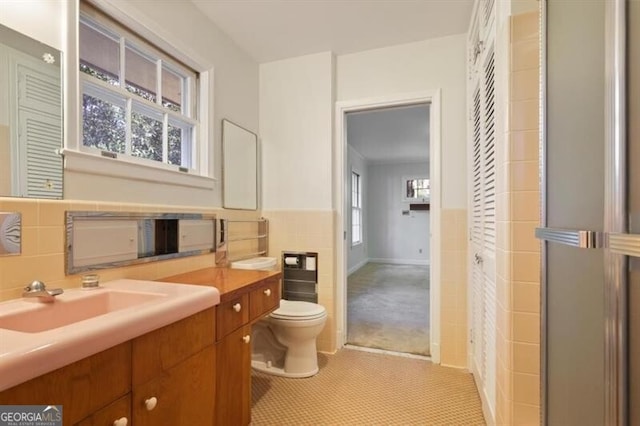 bathroom featuring tile patterned flooring, vanity, toilet, and tile walls