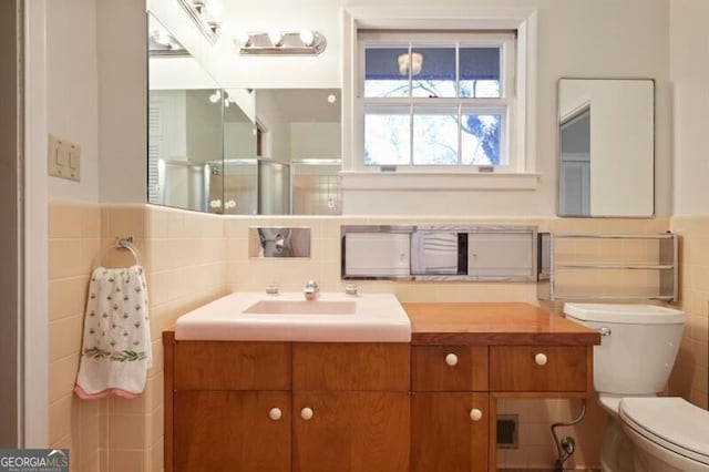 bathroom with vanity, toilet, an enclosed shower, and tile walls