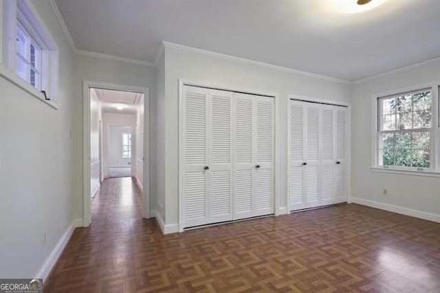 unfurnished bedroom featuring dark parquet flooring, multiple closets, and crown molding