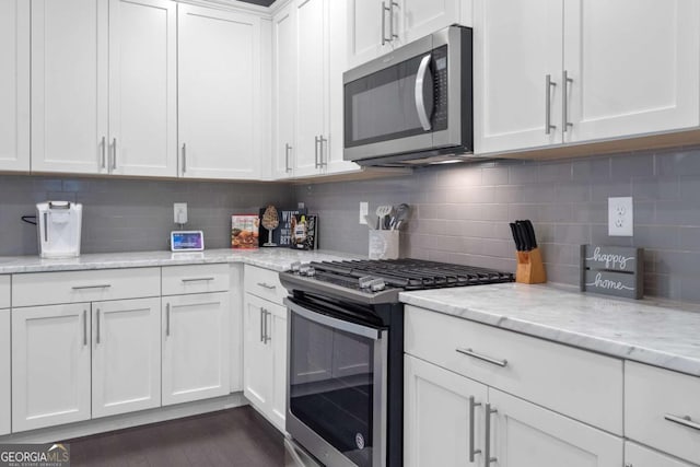 kitchen with backsplash, dark hardwood / wood-style floors, light stone countertops, white cabinetry, and stainless steel appliances