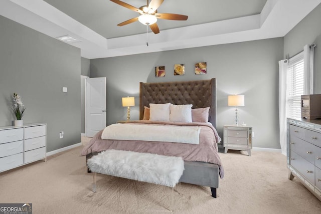 bedroom featuring light carpet, a tray ceiling, and ceiling fan