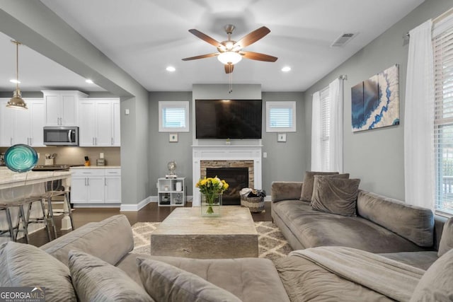 living room featuring a stone fireplace, ceiling fan, and dark wood-type flooring