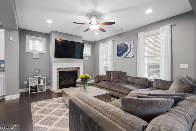 living room featuring dark hardwood / wood-style flooring, a stone fireplace, and ceiling fan