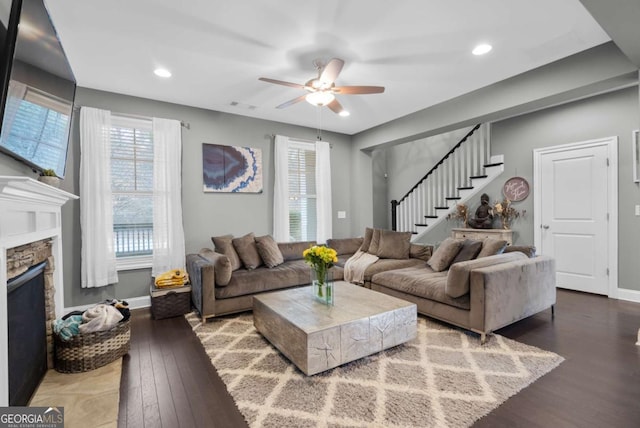 living room with ceiling fan, dark hardwood / wood-style floors, and a stone fireplace