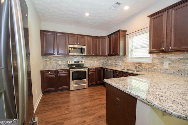 kitchen featuring stainless steel appliances, a sink, dark wood-style flooring, visible vents, and backsplash