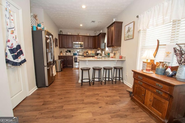 kitchen featuring a kitchen breakfast bar, kitchen peninsula, wood-type flooring, a textured ceiling, and appliances with stainless steel finishes