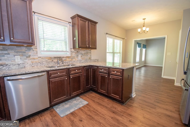 kitchen featuring backsplash, wood finished floors, a sink, a peninsula, and appliances with stainless steel finishes