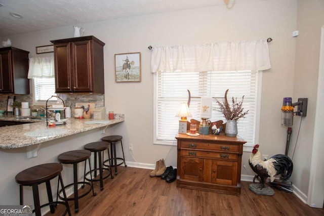 kitchen featuring backsplash, light stone countertops, a breakfast bar, and wood-type flooring