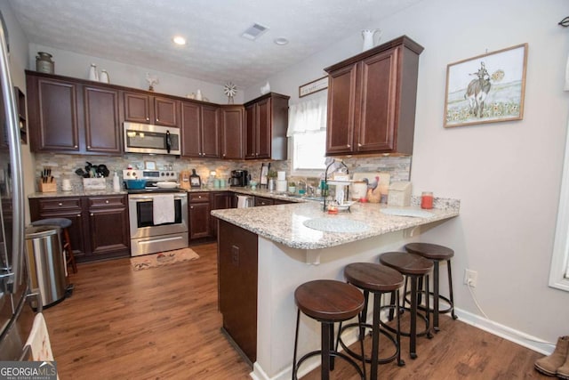 kitchen with a breakfast bar, light stone counters, appliances with stainless steel finishes, dark hardwood / wood-style flooring, and kitchen peninsula