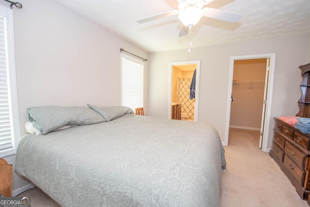 bedroom featuring a spacious closet, a ceiling fan, light carpet, a closet, and baseboards