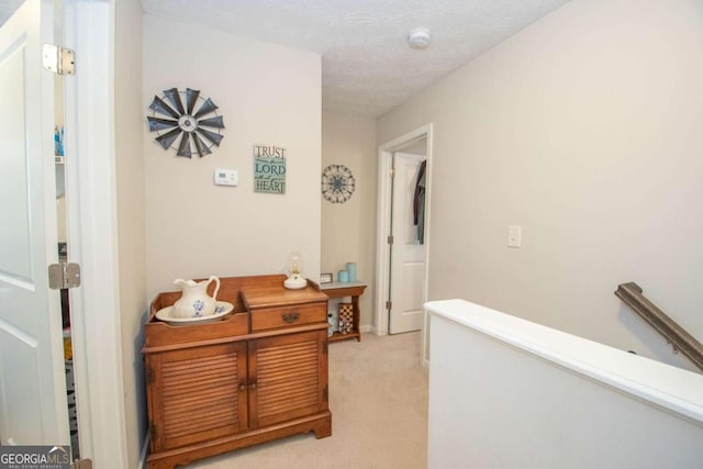 hallway with light carpet and a textured ceiling