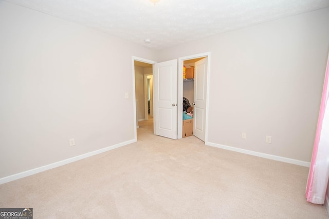unfurnished bedroom featuring light carpet, baseboards, a spacious closet, and a closet