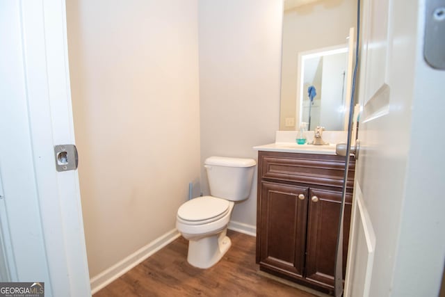 half bathroom featuring toilet, vanity, wood finished floors, and baseboards