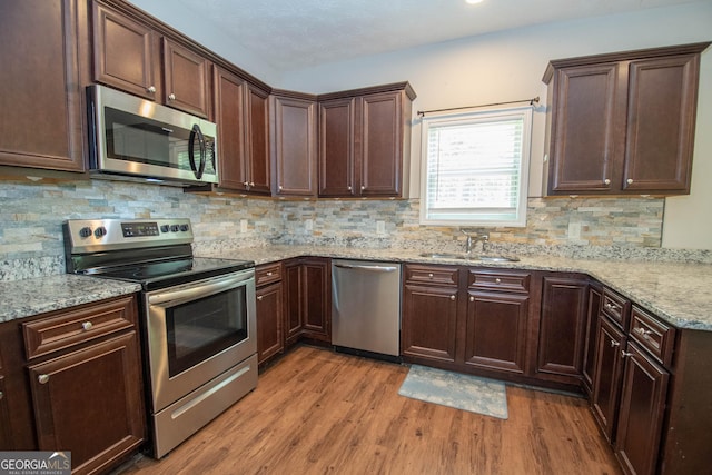 kitchen with light wood-style flooring, a sink, decorative backsplash, light stone countertops, and appliances with stainless steel finishes