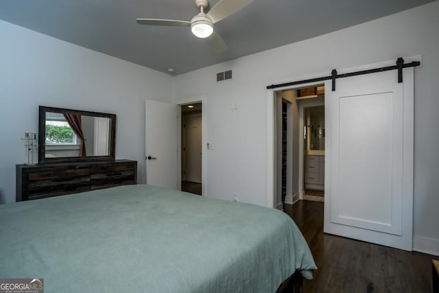 bedroom with connected bathroom, a barn door, ceiling fan, and dark hardwood / wood-style floors