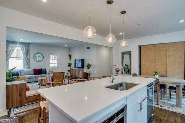 kitchen featuring pendant lighting, dishwasher, a kitchen island with sink, sink, and dark hardwood / wood-style flooring