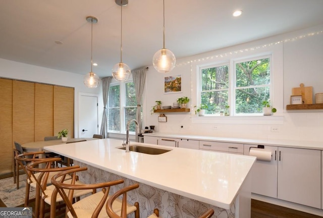 kitchen featuring white cabinets, sink, an island with sink, and hanging light fixtures