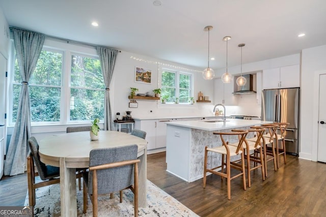 kitchen featuring stainless steel fridge, decorative light fixtures, white cabinetry, and wall chimney range hood