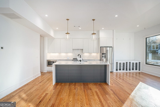 kitchen featuring pendant lighting, stainless steel appliances, an island with sink, light hardwood / wood-style floors, and white cabinets