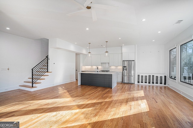 kitchen with a kitchen island with sink, hanging light fixtures, ceiling fan, stainless steel refrigerator with ice dispenser, and white cabinets