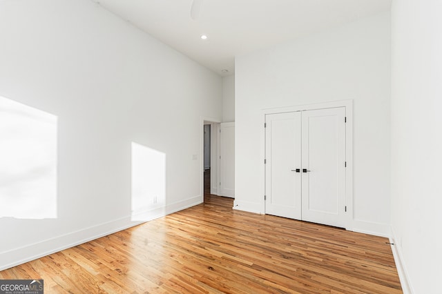 unfurnished bedroom with a high ceiling, light hardwood / wood-style floors, and a closet