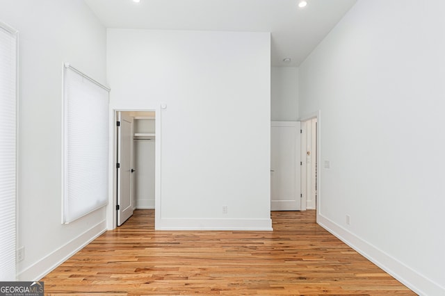 unfurnished bedroom with light hardwood / wood-style floors, a closet, and a towering ceiling