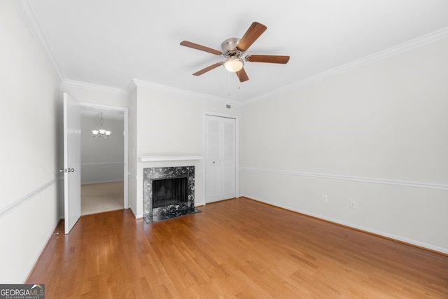 unfurnished living room featuring crown molding, a fireplace, ceiling fan with notable chandelier, and hardwood / wood-style flooring