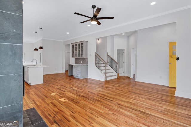 unfurnished living room featuring ceiling fan, light hardwood / wood-style floors, crown molding, and sink