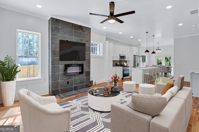 living room featuring ornamental molding, ceiling fan, sink, light hardwood / wood-style flooring, and a tiled fireplace