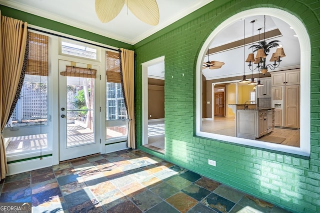 doorway with a notable chandelier, ornamental molding, and brick wall