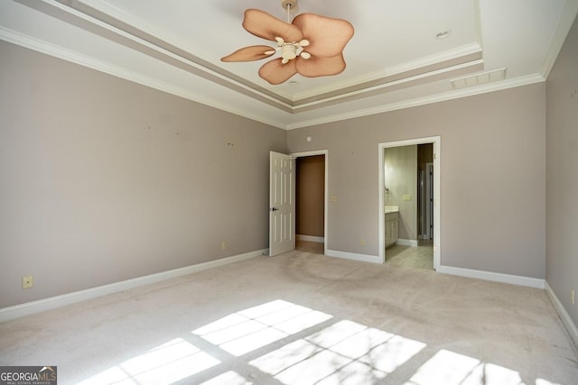 unfurnished bedroom featuring a raised ceiling, ensuite bathroom, crown molding, and light colored carpet