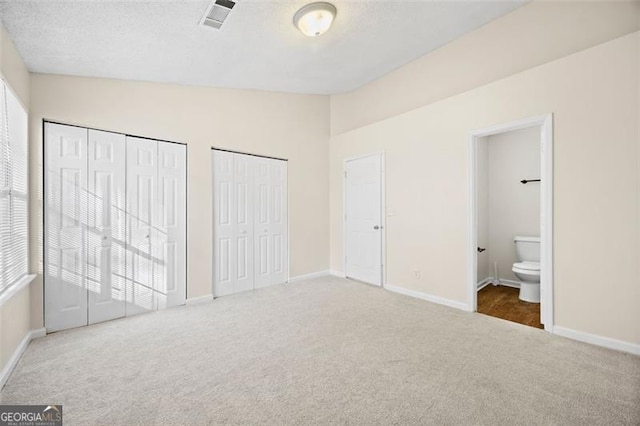 unfurnished bedroom featuring ensuite bath, carpet, two closets, and vaulted ceiling