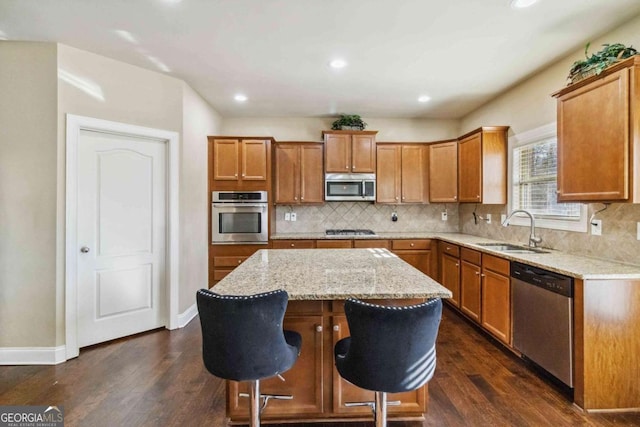 kitchen with sink, dark wood-type flooring, stainless steel appliances, light stone countertops, and a kitchen island