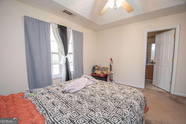 bedroom with ceiling fan, light colored carpet, and connected bathroom