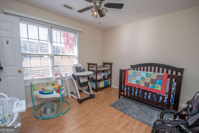 bedroom featuring light wood-type flooring, a nursery area, and ceiling fan