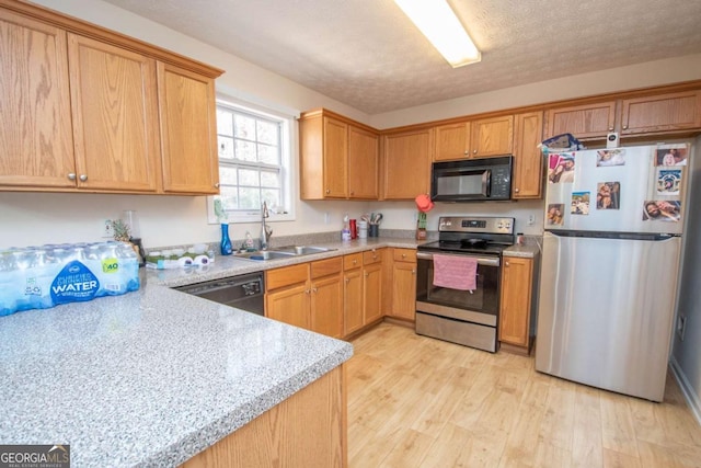 kitchen featuring appliances with stainless steel finishes, a textured ceiling, light hardwood / wood-style floors, and sink