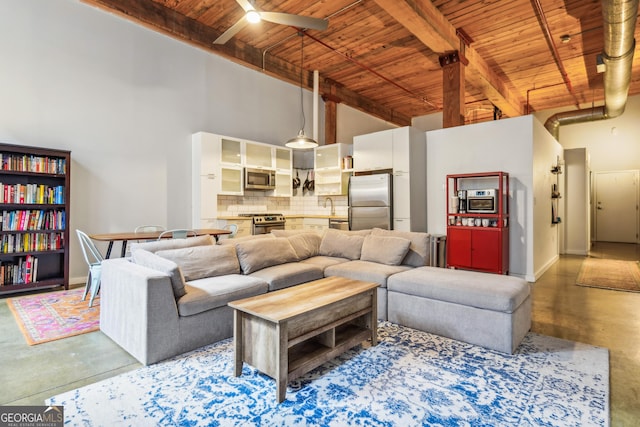 living room with a towering ceiling, ceiling fan, beam ceiling, wooden ceiling, and concrete floors