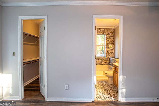 unfurnished bedroom featuring dark wood-type flooring, a walk in closet, crown molding, connected bathroom, and a closet