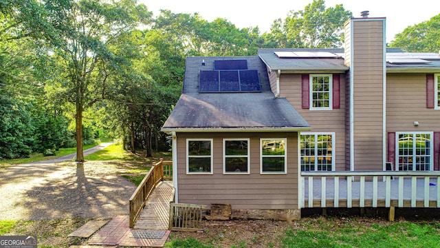 rear view of property featuring solar panels and a deck