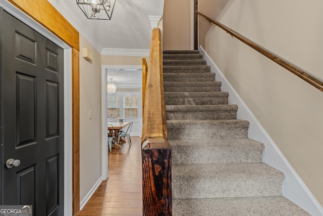 staircase with a textured ceiling, wood-type flooring, a notable chandelier, and ornamental molding