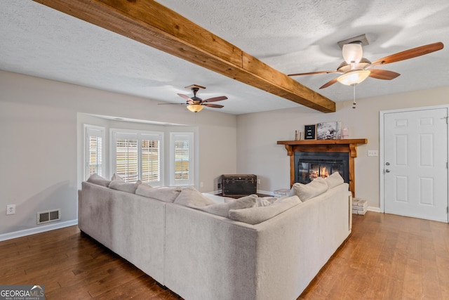 living room with beam ceiling, ceiling fan, wood-type flooring, and a textured ceiling