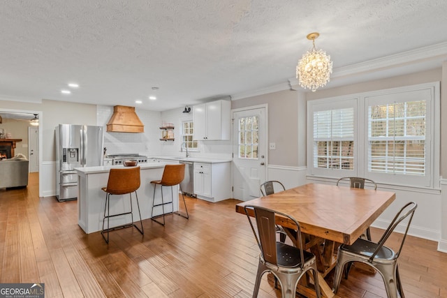 dining area featuring light wood-type flooring, ornamental molding, and a textured ceiling