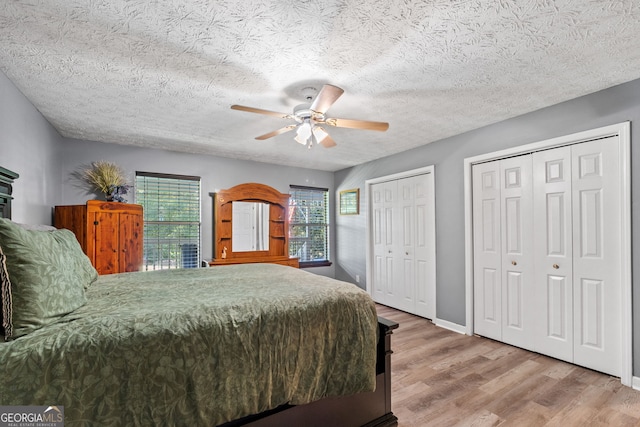 bedroom with wood-type flooring, a textured ceiling, two closets, and ceiling fan