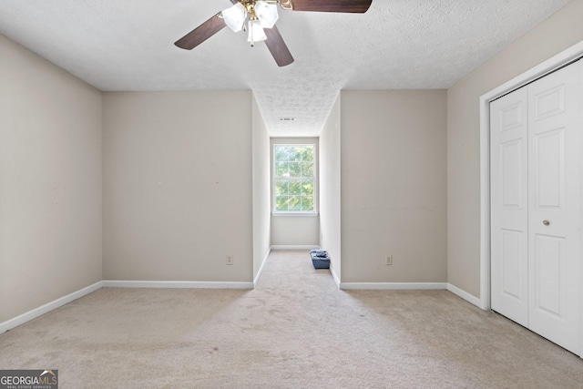 unfurnished bedroom with ceiling fan, a closet, light carpet, and a textured ceiling