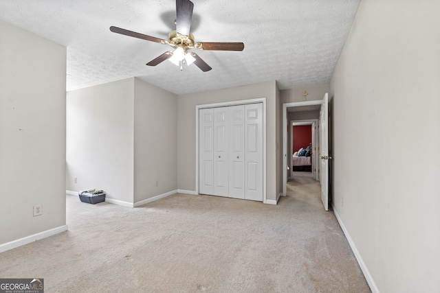 unfurnished bedroom with ceiling fan, a closet, light carpet, and a textured ceiling